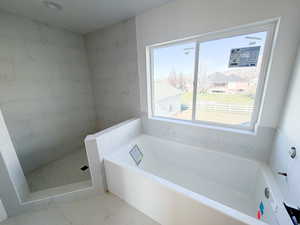 Bathroom featuring a bath, walk in shower, and marble look tiles