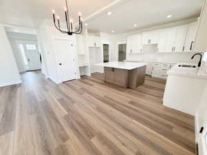 Modern kitchen featuring white cabinetry, light countertops, a central island, wood-finish flooring, and a contemporary chandelier