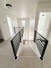 Staircase featuring modern black metal railings, light-toned carpeted treads, and wood-finish flooring at the bottom landing
