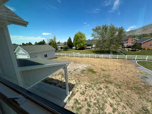 Expansive undeveloped backyard featuring a white picket fence, mature trees, and mountain scenery