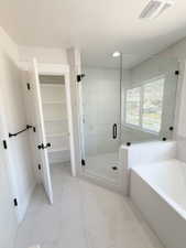 Modern bathroom featuring a glass-enclosed shower with tile surround, a built-in bathtub, and a separate linen closet with shelving