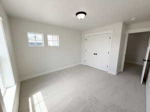 Neutral-toned bedroom featuring twin windows, light-colored carpeting, white baseboards, and a double-door closet with dark hardware
