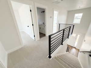 Upper-level landing featuring a modern horizontal metal railing system and light-toned carpet flooring