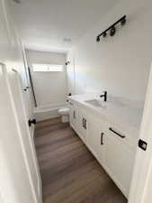 Bathroom featuring a white subway tile tub surround, white vanity with black hardware, white countertop, wood-finish flooring, and a black-finish vanity light fixture