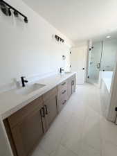 Modern bathroom featuring a dual vanity with light wood-finish cabinetry, speckled white countertops, and black fixtures