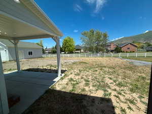 Expansive backyard featuring a concrete patio, covered porch area with recessed lighting, and a white fence bordering the property