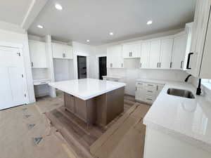 Two tone kitchen with light stone counters, wood finished floors, dual tone cabinets, recessed lighting, and a kitchen island