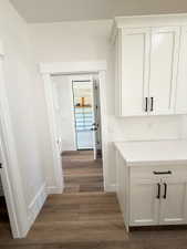 White shaker-style cabinetry with black hardware, light-toned countertop, and wood-finish flooring