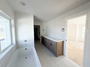 Full bathroom featuring a garden tub, double vanity, and light marble finish flooring
