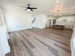 Spacious open-concept interior featuring wood-finish flooring, a contemporary ceiling fan, recessed lighting, and a modern chandelier
