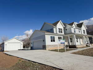 View of front facade featuring board and batten siding, stone siding, covered porch, a shingled roof, and a detached garage