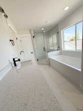 Contemporary bathroom featuring a spacious white countertop with an integrated sink and black faucet, a large soaking tub with a tiled surround, a glass-enclosed shower with white subway tile, a wide window, and recessed ceiling lighting