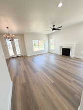 Spacious living area featuring wood-finish flooring, a fireplace with a white mantel, and vaulted ceilings with recessed lighting