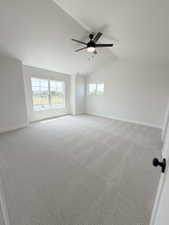Spacious room featuring vaulted ceilings, a ceiling fan with light, multiple windows, and patterned carpeting
