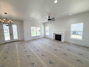Unfurnished living room featuring a fireplace, a chandelier, a ceiling fan, and healthy amount of natural light