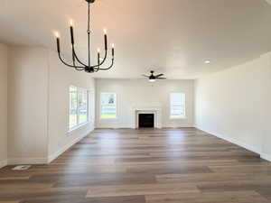 Spacious room featuring wood-finish flooring, a white mantel fireplace, multiple windows with white trim, a black ceiling fan, and a black chandelier