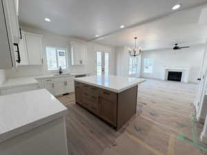 Dual tone kitchen featuring a kitchen island, two tone cabinets, a fireplace, suspended lighting, and light wood-style floors