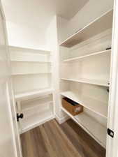 Walk-in pantry featuring extensive white shelving, wood-finish flooring, and a modern black door handle