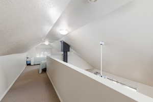 Hallway with a textured ceiling, light carpet, and lofted ceiling
