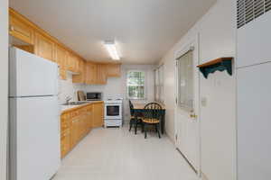 Kitchen featuring white appliances, light countertops, a heating unit, decorative backsplash, and light brown cabinetry