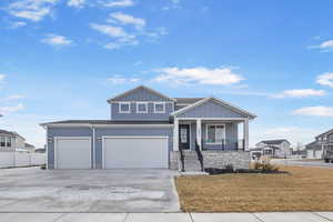 View of front of house featuring covered porch, concrete driveway, an attached garage, stone siding, and board and batten siding