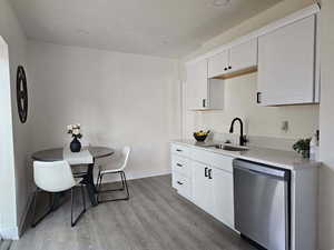 Kitchen featuring dishwasher, light wood-style floors, white cabinets, light stone counters, and a textured ceiling