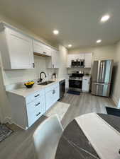 Kitchen featuring light wood-type flooring, white cabinetry, stainless steel appliances, light stone countertops, and recessed lighting