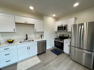 Kitchen featuring stainless steel appliances, white cabinetry, light wood-type flooring, light stone counters, and recessed lighting