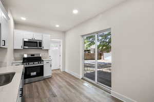 Kitchen featuring stainless steel appliances, light wood-style floors, white cabinetry, recessed lighting, and light stone counters