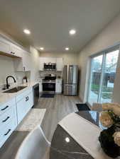 Kitchen with stainless steel appliances, white cabinets, light wood-style flooring, and recessed lighting