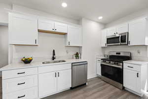 Kitchen featuring appliances with stainless steel finishes, white cabinetry, light wood-type flooring, recessed lighting, and light stone countertops