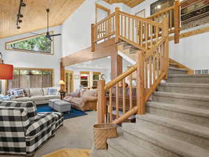 Living area with track lighting, wood ceiling, stairs, carpet flooring, and high vaulted ceiling
