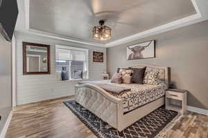 Bedroom with a tray ceiling, wood finished floors, crown molding, and wooden walls