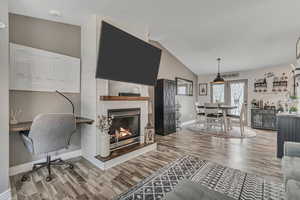 Living room with wood finished floors, a fireplace, vaulted ceiling, and an office area