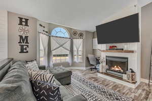 Living area featuring wood finished floors, a glass covered fireplace, and lofted ceiling