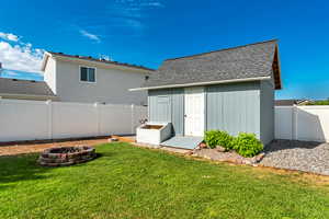 Back of house with a fire pit, roof with shingles, a fenced backyard, and a storage unit