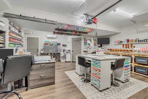 Office with light wood-type flooring, a garage, and a wall unit AC