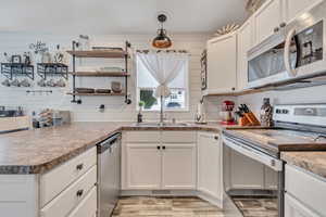 Kitchen with appliances with stainless steel finishes, white cabinetry, light wood finished floors, pendant lighting, and a peninsula