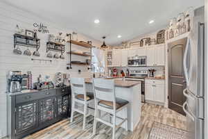 Kitchen with appliances with stainless steel finishes, white cabinetry, lofted ceiling, light wood-style flooring, and a breakfast bar