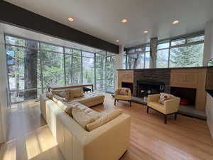 Living room with light wood-style floors, a fireplace, recessed lighting, and a wall of windows