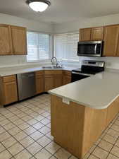 Kitchen featuring a peninsula, appliances with stainless steel finishes, light tile patterned floors, light countertops, and a textured ceiling