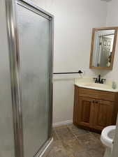 Bathroom featuring vanity, a shower stall, and dark stone finish floors