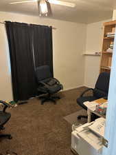 Home office featuring a textured ceiling, carpet flooring, and a ceiling fan