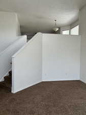 Unfurnished room featuring dark colored carpet, a textured ceiling, and stairs