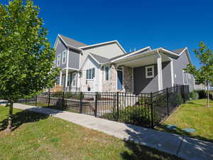 View of front of home featuring a fenced front yard, a porch, stone siding, and roof with shingles