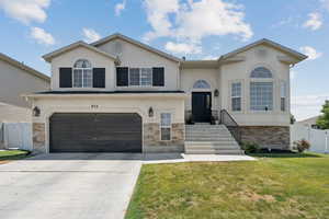 View of front facade featuring stone siding, driveway, a garage, and stucco siding