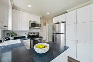 Kitchen featuring stainless steel appliances, a peninsula, tasteful backsplash, white cabinets, and crown molding