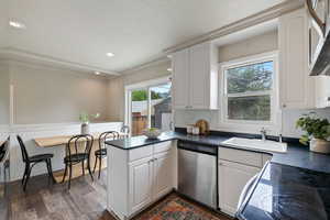 Kitchen with stainless steel appliances, a peninsula, dark countertops, white cabinetry, and ornamental molding