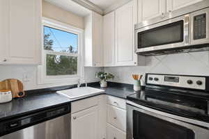 Kitchen with appliances with stainless steel finishes, dark countertops, and white cabinets