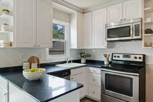 Kitchen featuring open shelves, stainless steel appliances, white cabinets, a peninsula, and tasteful backsplash